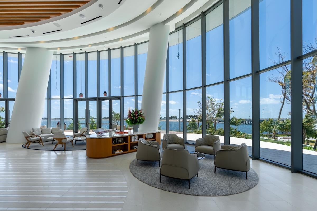 Sunlit waterfront lobby of a luxury managed condominium in Brickell, Miami, with floor-to-ceiling windows overlooking Biscayne Bay